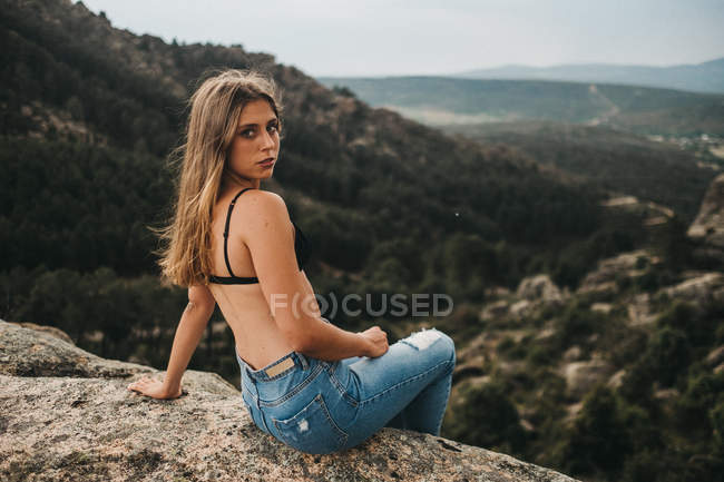 Mujer en sujetador sentado en las rocas - foto de stock