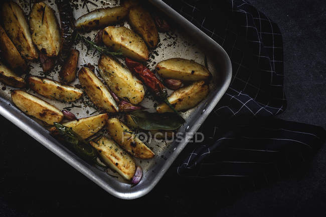 Roasted golden crunchy potato wedges in baking pan on black surface — Stock Photo