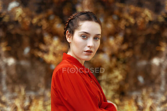 Side view of crop attractive lady in red shirt and hairstyle crossing hands and looking at camera — Stock Photo