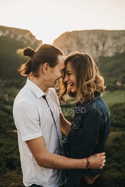 Cute couple hugging and toughing foreheads while standing on background of beautiful valley and mountains — Stock Photo