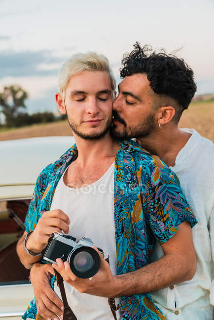 Besar a los hombres enamorados abrazando tiernamente mientras están de pie con la cámara fotográfica en la naturaleza disfrutando de viajes - foto de stock