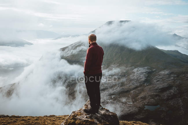 Escursionista irriconoscibile in piedi sul bordo della montagna tra le nuvole sulle isole Feroe — Foto stock