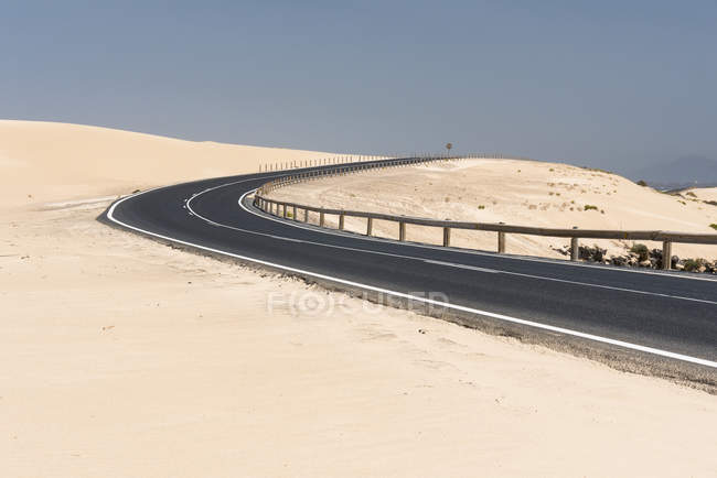 Larga carretera recta sobre llanura con dunas de arena, Islas Canarias - foto de stock