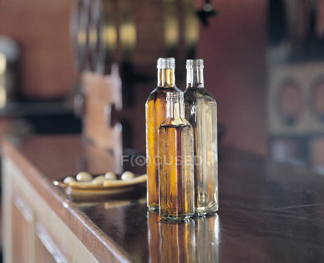 Glass bottles with yellow liquid standing on counter near plate with snacks on blurred background of bar — Stock Photo