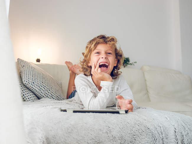 Fröhlicher Junge mit digitalem Tablet auf Couch liegend — Stockfoto