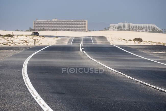 Autostrada nel deserto di Fuerteventura con edifici cittadini su sfondo sfocato, Isole Canarie — Foto stock