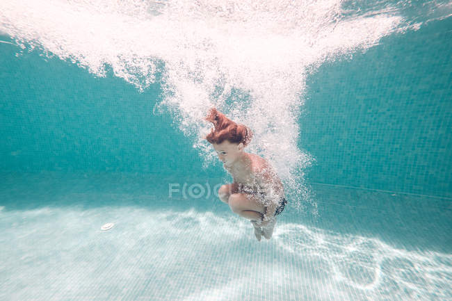 Boy in swimming trunks diving into transparent blue pool water — Stock Photo