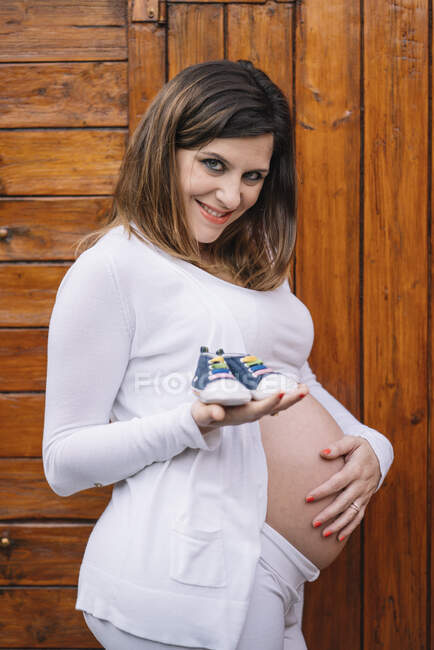Mujer bonita embarazada muestra los zapatos de su hijo. - foto de stock