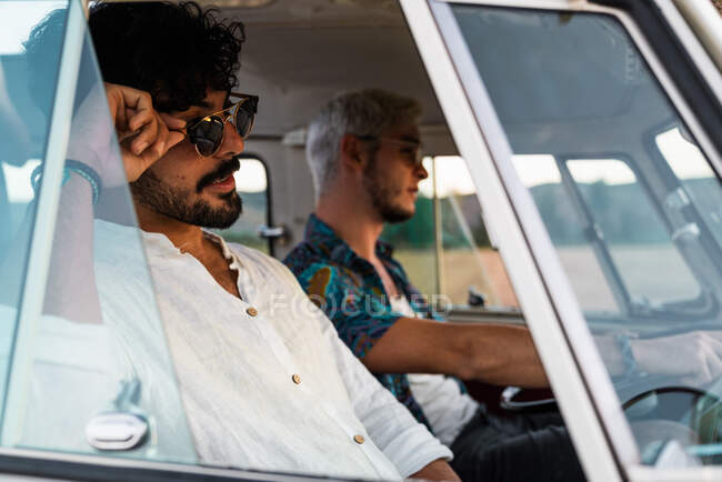 Двоє красивих чоловіків сміються і дивляться геть, приймаючи один одного і катаючись в ретро-автомобілі під час поїздки — стокове фото