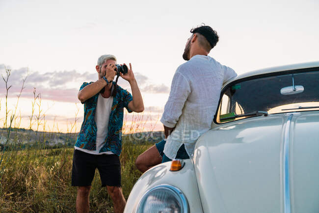 Casual homem de camisa usando câmera fotográfica e imaginando o homem com carro na paisagem do campo no verão — Fotografia de Stock