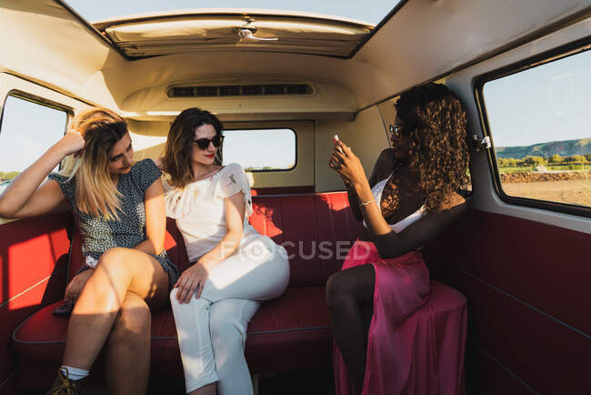 Три веселые молодые женщины сидят в винтажном фургоне и позируют для селфи, путешествуя вместе — стоковое фото