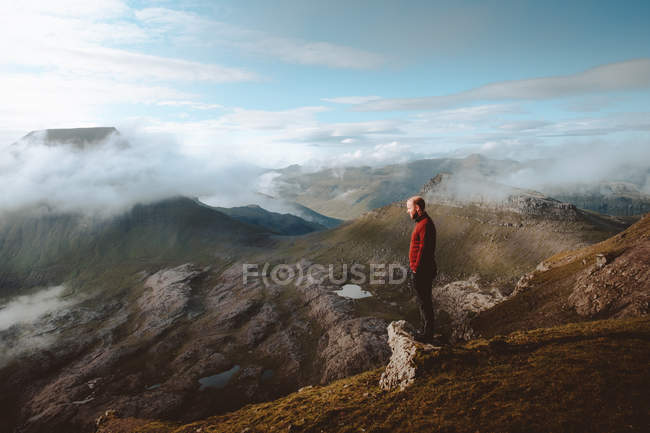 Excursionista de pie en el borde de la montaña y mirando a la vista en las Islas Feroe - foto de stock