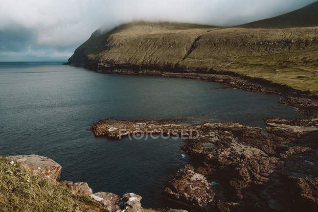 Océan et falaise rocheuse verte sur les îles Feroe — Photo de stock