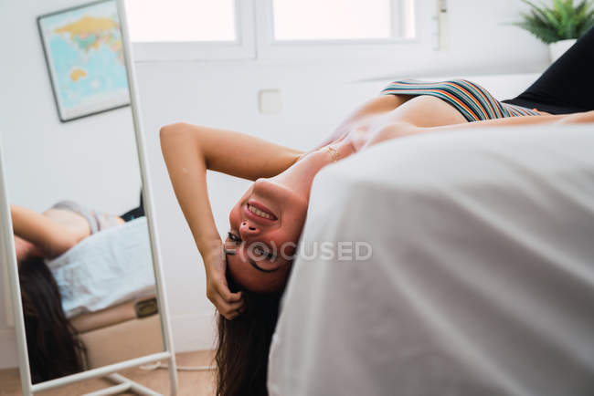 Jovem mulher brincalhão deitada na cama perto do espelho e olhando para a câmera — Fotografia de Stock