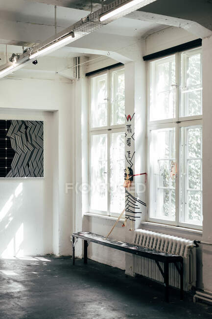 Довга чорна лавка, що стоїть на підлозі біля прикрашеного стовпа і великих вікон у світлій кімнаті — стокове фото