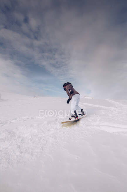 ¿Mujer irreconocible usando ropa de abrigo y snowboard con munición especial deslizándose cuesta abajo? sobre fondo nublado del cielo - foto de stock