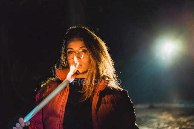 Jovem mulher bonita de pé com iluminação tocha na parte de trás iluminado à noite . — Fotografia de Stock