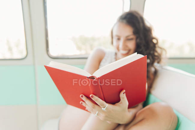 Primer plano de la mujer sentada dentro de la caravana y leyendo libro - foto de stock