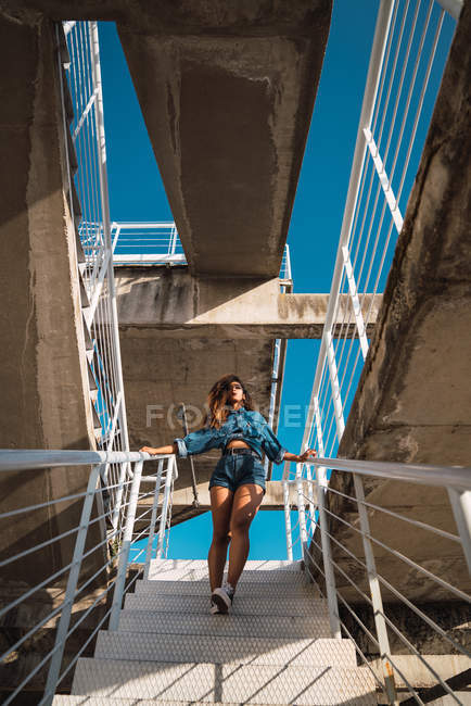 Jovem afro-americana em roupas jeans indo para baixo em escadaria de metal na rua à luz do dia — Fotografia de Stock