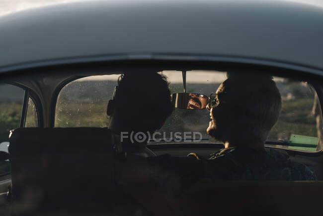 Rückansicht von zwei nicht wiedererkennbaren jungen Männern, die sich umarmen und die Natur bewundern, während sie im Retro-Auto sitzen — Stockfoto