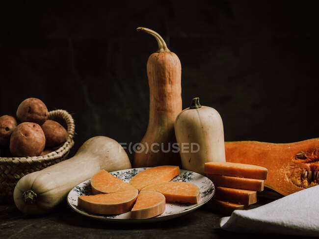 Beautiful warm arrangement of ripe butternut squashes on table with tiny tomatoes and plate with slices — Stock Photo