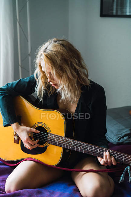 Jovem loira tocando guitarra na cama em casa — Fotografia de Stock