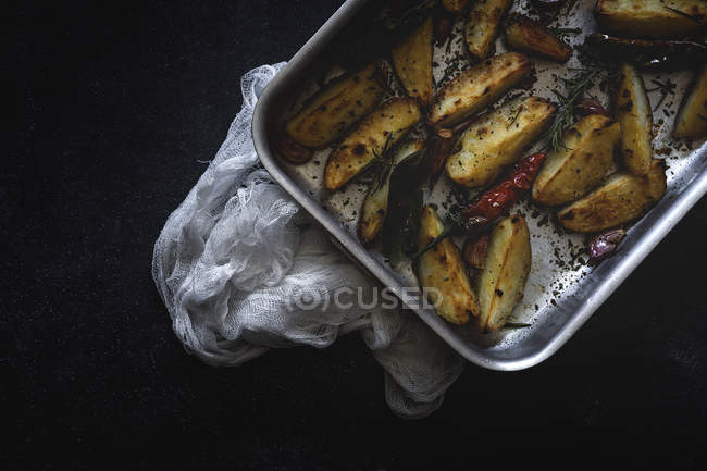 Cuñas de patata crujientes doradas tostadas en bandeja para hornear en la superficie negra - foto de stock