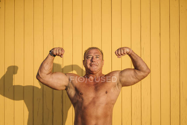 Muscular older man poses yellow background — Stock Photo
