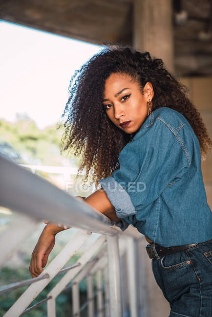 Young woman leaning on railing on balcony and looking at camera — Stock Photo