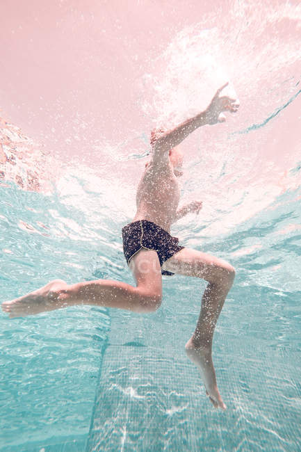 Мальчик в плавках в прозрачном бирюзовом бассейне — стоковое фото