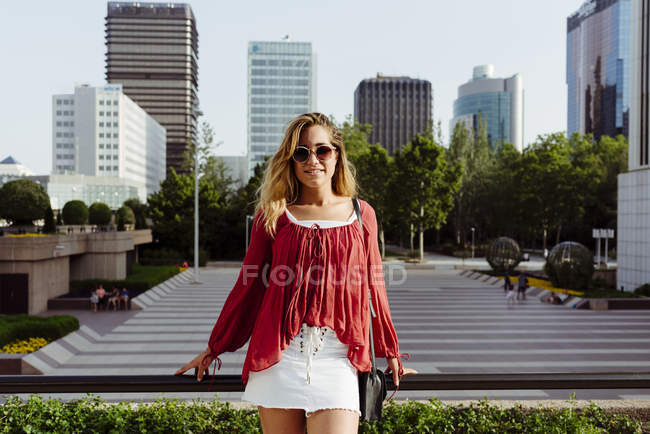 Приваблива молода жінка спирається на поручень на тлі хмарочосів в місті — стокове фото