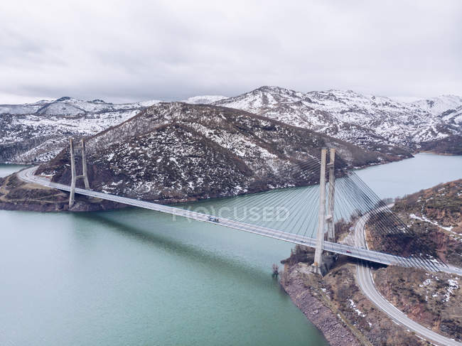 Pintoresca vista en dron del largo puente que cruza un hermoso río entre magníficas colinas nevadas de Asturias, España - foto de stock