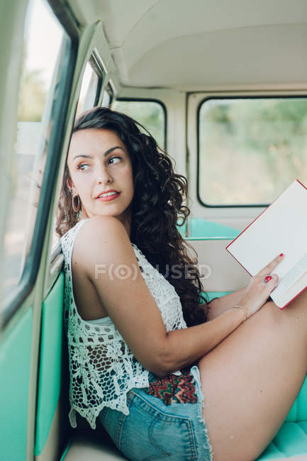 Junge Frau sitzt in Wohnwagen und liest mit Buch — Stockfoto