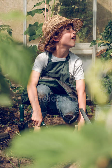 Boy in straw hat working in greenhouse with garden tools — Stock Photo