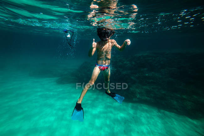 Неузнаваемый мальчик ныряет с маской в море и показывает большой палец вверх — стоковое фото