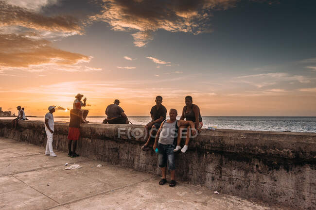 LA HABANA, CUBA - MAY 1, 2018: Cuban city dwellers chilling on pedestrian concrete waterfront on background of sunset sky, — Stock Photo
