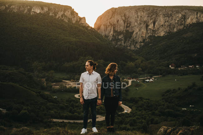 Красивый мужчина и красивая женщина смотрят в сторону, стоя на фоне удивительных гор и долины вместе — стоковое фото