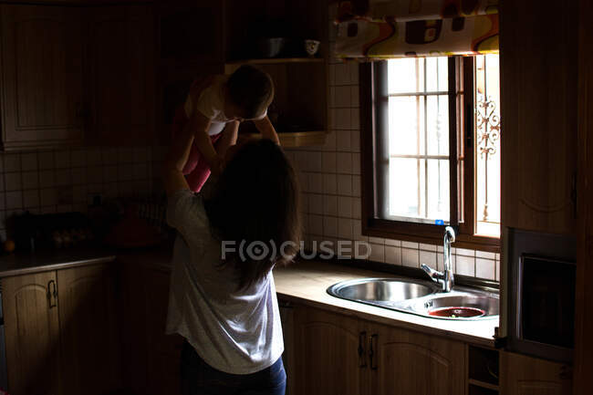 Жінка на кухні грає з дитиною — стокове фото