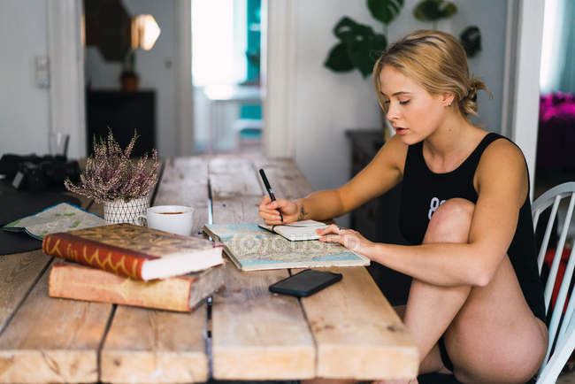 Mujer rubia sentada a la mesa con libros, mapa y café y viaje de planificación - foto de stock