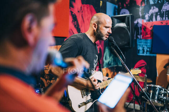 Two musicians playing guitar and singing on stage with drums placed near on background of photos on wall — Stock Photo