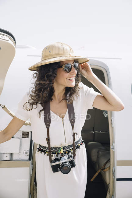 Viajero femenino sonriente con cámara fotográfica que sale del avión a la llegada al aeropuerto - foto de stock