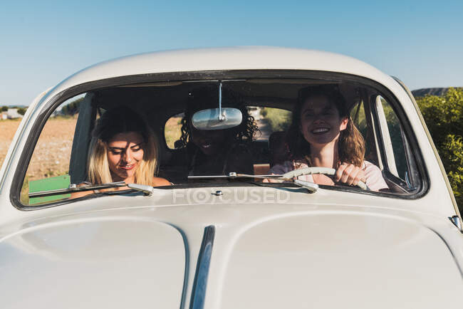 Grupo de mulheres multiétnicas felizes no carro dirigindo juntos na luz solar brilhante e rindo — Fotografia de Stock