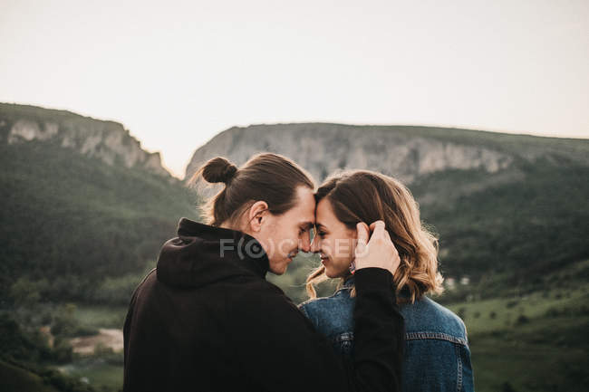 Bonito casal abraço e testa endurecida enquanto sentado em encosta rochosa no fundo do belo vale e montanhas — Fotografia de Stock