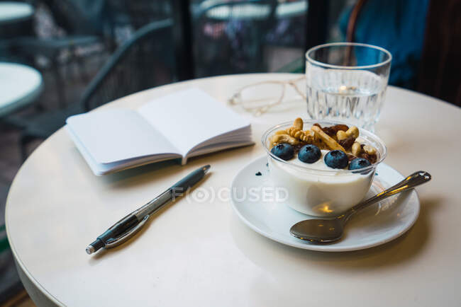 Fruit dessert and glass of water placed on white table near opened notebook and pen — Stock Photo