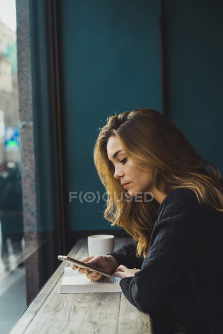 Mujer joven usando teléfono inteligente en la cafetería - foto de stock