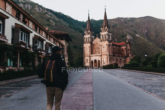 Rückansicht eines Mannes mit Rucksack, der auf der Straße der kleinen Bergstadt in Richtung schöne Kirche läuft — Stockfoto