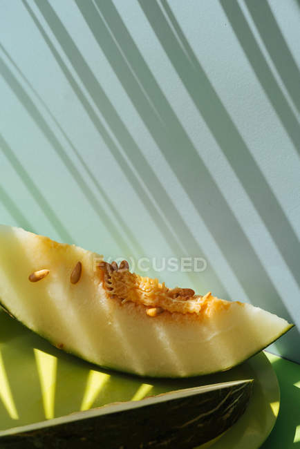 Tranches de melon frais sur fond bleu et vert avec des ombres de feuilles de palmier — Photo de stock