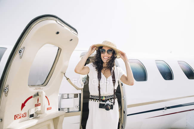 Viajante sorridente do sexo feminino com câmera de fotos saindo do avião na chegada ao aeroporto — Fotografia de Stock