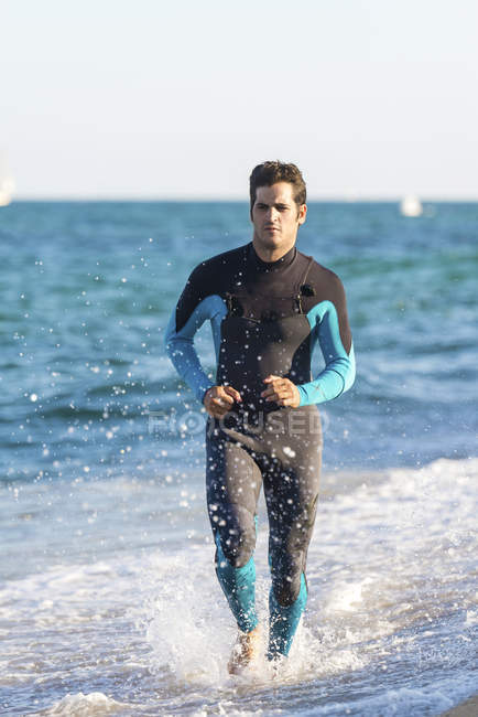 Surfista con neopreno corriendo por la playa - foto de stock