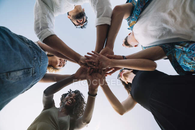 From below shot of young friends laughing and holding hands together while standing on background of clear sky — Stock Photo